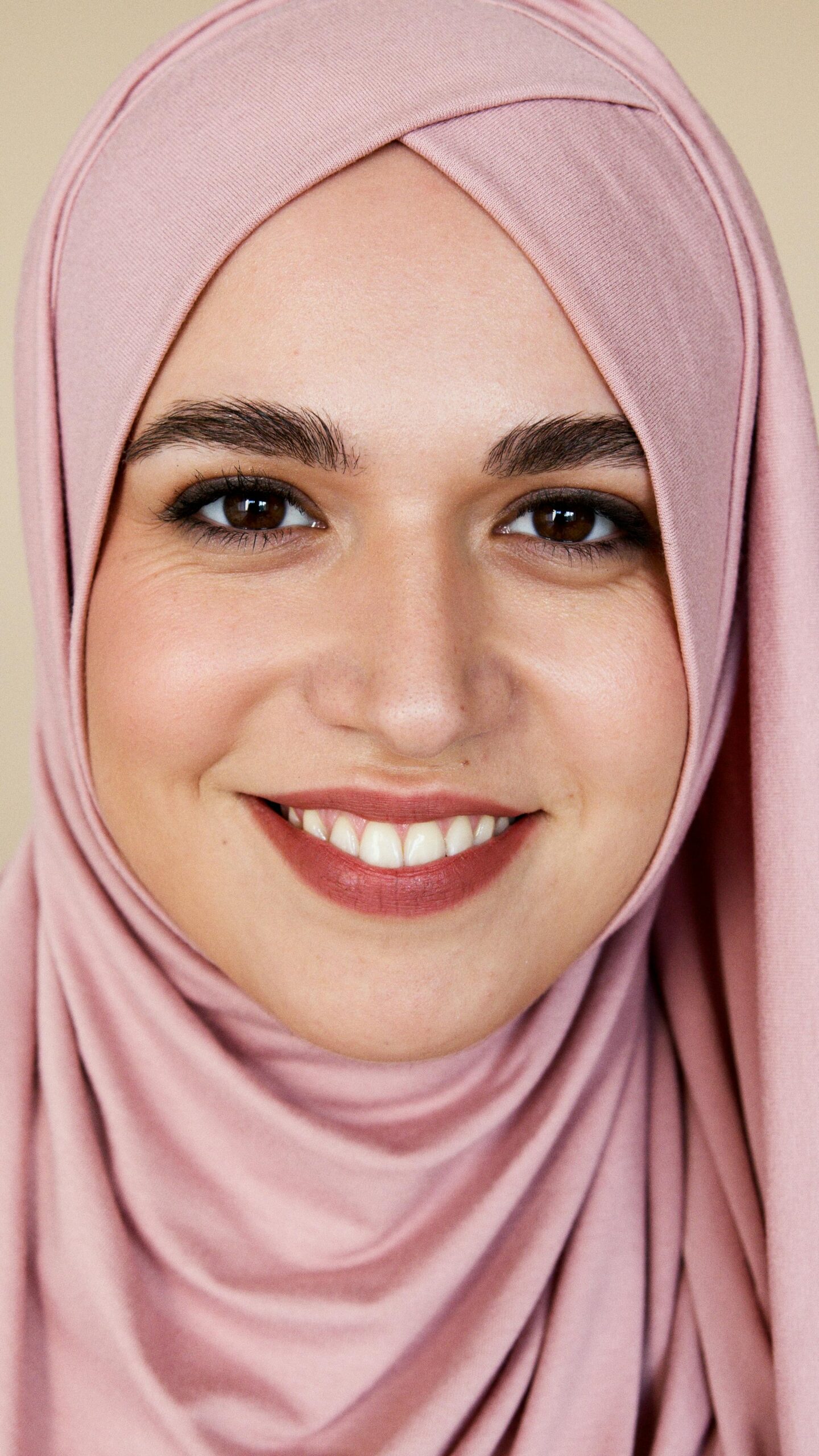 Close-up portrait of a smiling woman in a pink hijab, showcasing cultural beauty.